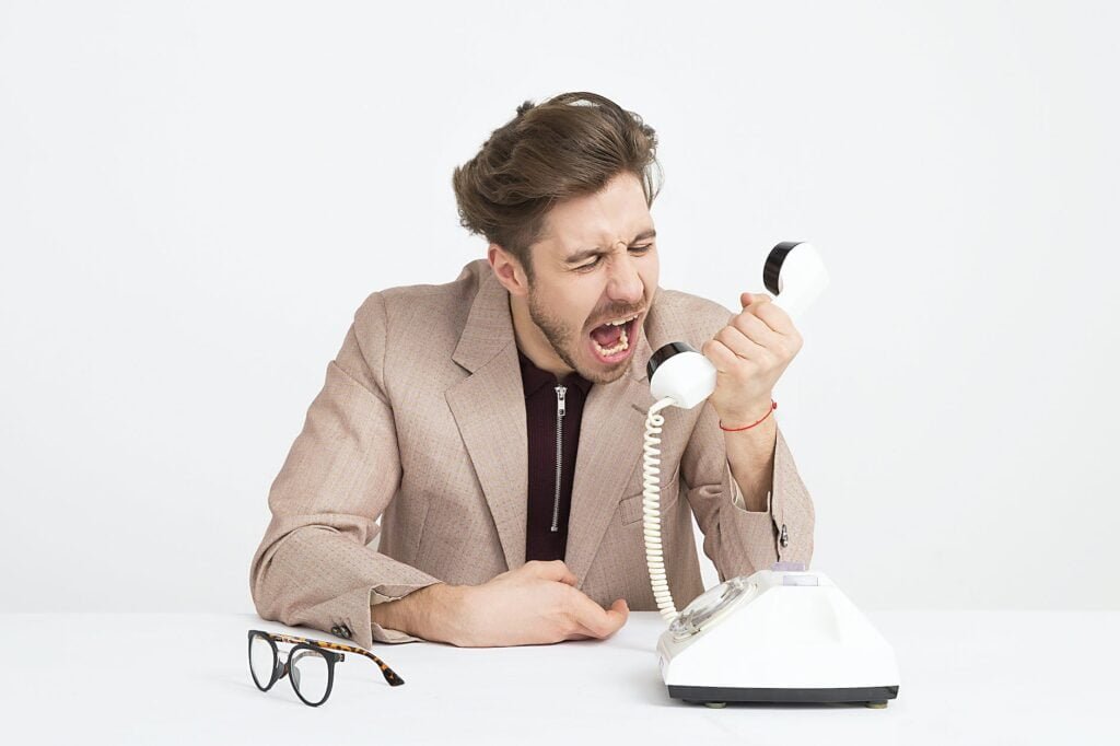 man wearing brown suit jacket mocking on white telephone because outlook's junk mail filter is not working.